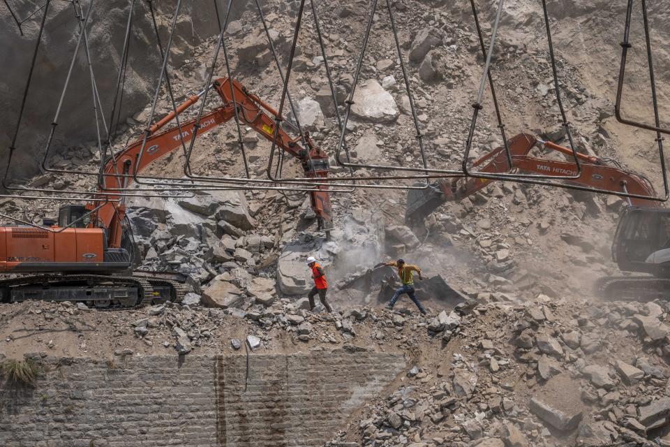 Rescue workers run for cover as earth movers dig through rubble of a collapsed tunnel in Ramban district, south of Srinagar, Indian controlled Kashmir, Friday, May 20, 2022. An official in Indian-controlled Kashmir said Friday that 10 workers were trapped after part of a road tunnel collapsed in the Himalayan region. (AP Photo/Dar Yasin)