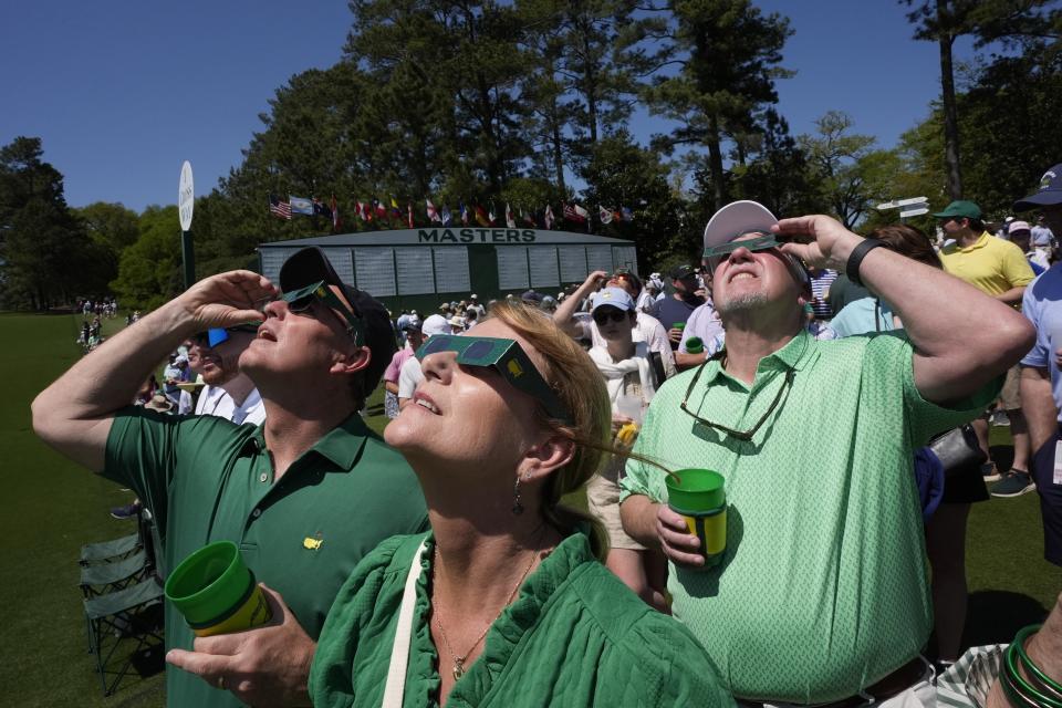 Patrons look up at the sun during an solar eclipse during a practice round in preparation for the Masters golf tournament at Augusta National Golf Club Monday, April 8, 2024, in Augusta, Ga. (AP Photo/George Walker IV)