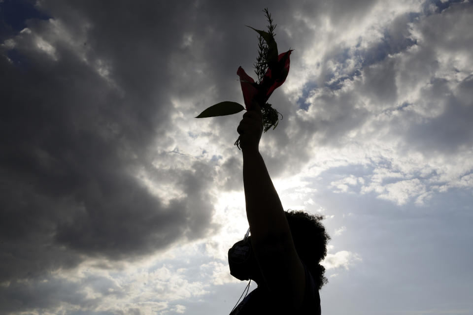 A women's movement activist holds flowers in her hand, during a protest against the government's inefficiency in the face of the COVID-19 pandemic and the ongoing police brutality against blacks, in Brasilia, Brazil, Thursday, July 2. 2020. (AP Photo/Eraldo Peres)