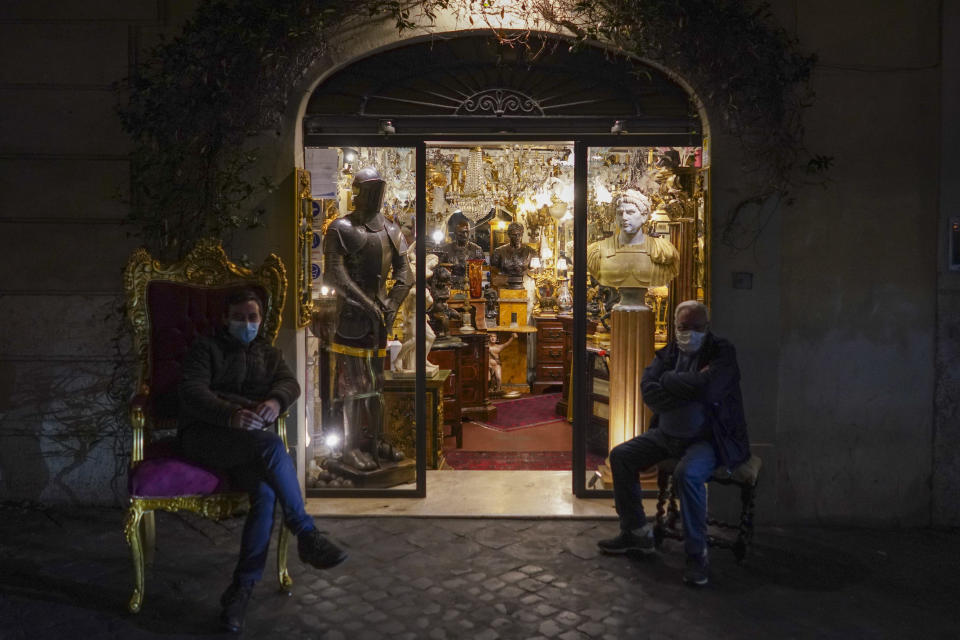 The owners of an antiquities store sit outside their shop, in Rome, Wednesday, Nov. 4, 2020. Italy’s one-day new caseload of confirmed coronavirus infections has again topped 30,000, with the northern region of Lombardy accounting for more than one-quarter of the day’s cases in Health Ministry figures released on Wednesday. (AP Photo/Andrew Medichini)