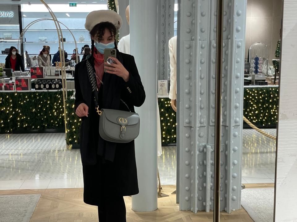 Amber Lucas takes a selfie in a store mirror while trying a designer handbag for size. She is wearing a face mask because of Covid.