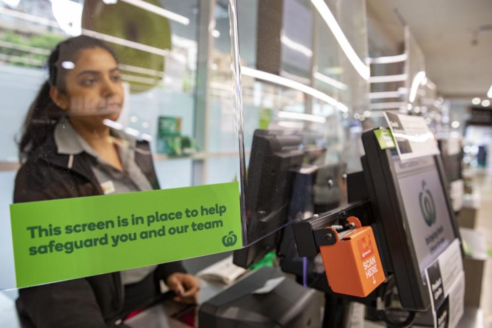 A Woolworths worker is seen looking out from behind a screen installed to protect workers amid the coronavirus pandemic.