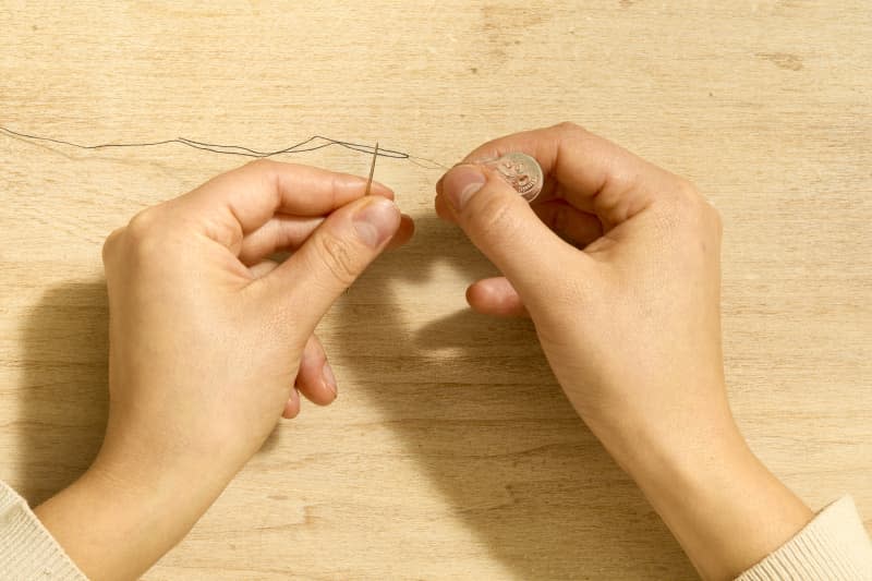 Overhead shot of two hands using a needle threader to thread a needle.