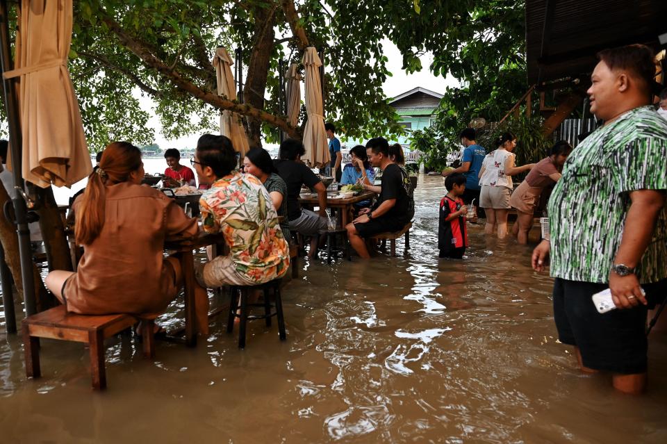 This photo taken on October 7, 2021, shows people enjoying dinner at the Chaopraya Antique Cafe, as flood water from the Chao Phraya River surges into the restaurant, in Nonthaburi province north of Bangkok.