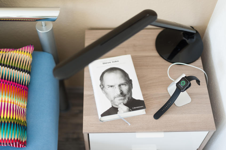 Ostfildern, Germany - May 21, 2015: An Apple Watch is being loaded on the bedside table using a stylish stand by manufacturer Spigen next to the biography of Steve Jobs, the innovative long term leader of Apple Computer Inc. The Apple smartwatch should be charged every day since the battery does not last much longer, most people use to charge their watch during night time therefore. 
