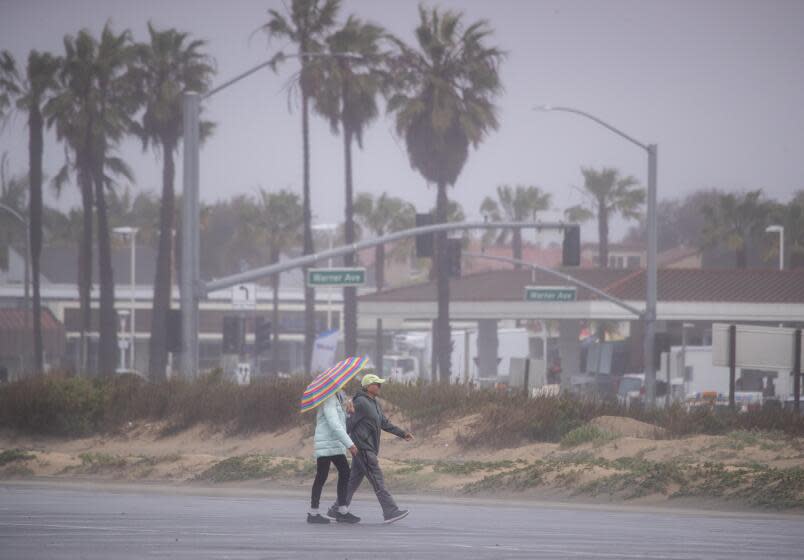 Huntington Beach, CA - March 15: A walk with an umbrella amidst the rain at Bolsa Chica State Beach, which is partially closed after both sides of PCH were closed due to flooding between Warner Avenue and Seapoint Street in Huntington Beach Wednesday, March 15, 2023. Re-opening times were not announced. (Allen J. Schaben / Los Angeles Times)