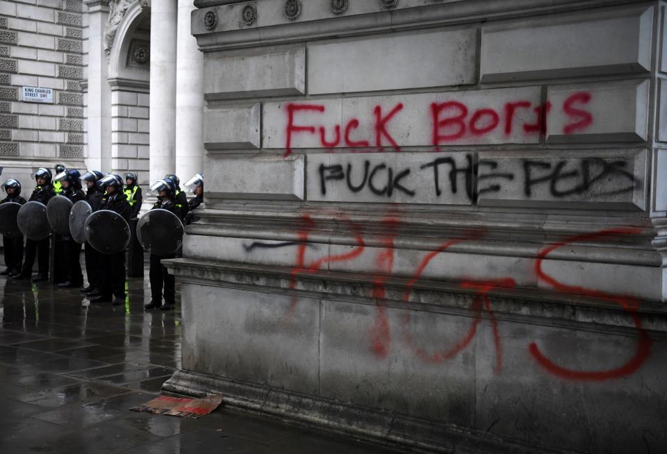 Police officers in riot gear stand on duty by anti-government graffiti daubed on the the Foreign Office in central London on June 6, 2020, during a demonstration organised to show solidarity with the Black Lives Matter movement in the wake of the killing of George Floyd, an unarmed black man who died after a police officer knelt on his neck in Minneapolis. - The United States braced Friday for massive weekend protests against racism and police brutality, as outrage soared over the latest law enforcement abuses against demonstrators that were caught on camera. With protests over last week's police killing of George Floyd, an unarmed black man, surging into a second weekend, President Donald Trump sparked fresh controversy by saying it was a "great day" for Floyd. (Photo by DANIEL LEAL-OLIVAS / AFP) (Photo by DANIEL LEAL-OLIVAS/AFP via Getty Images)