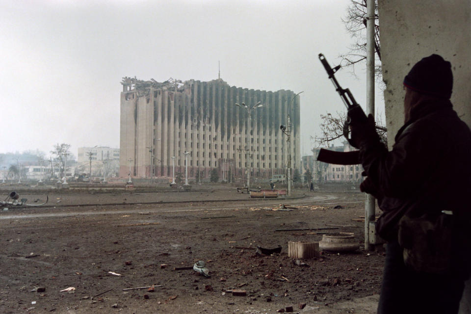 A Chechen fighter takes cover from sniper fire in front of the presidential palace, which was destroyed.