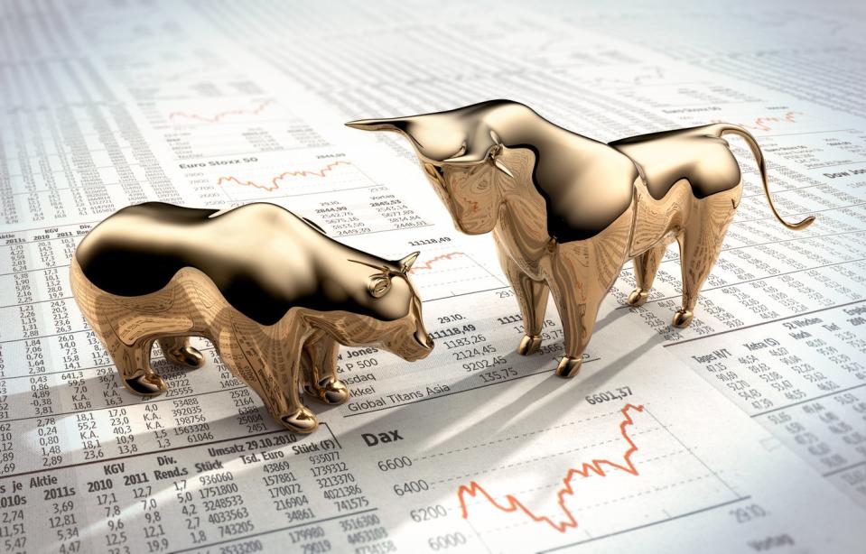 Miniature golden bull and bear figurines placed on top of a paper showing stock and finance information.