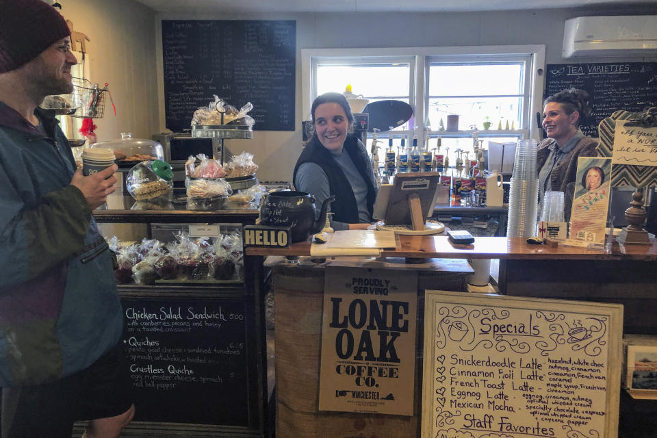 Behind the counter, Kathryn Philips, left, and Jessica Sullivan chat with a customer at Back Street Brews in Lovettsville, Va., on Dec. 16, 2021. The cafe is the social hub in a polarized town and a place where neighbors across the political divide gather without the rancor that rages across America's public square. (AP Photo/Cal Woodward)