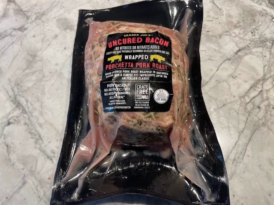Black shrink-wrapped Trader Joe's uncured bacon porchetta roast on a gray counter