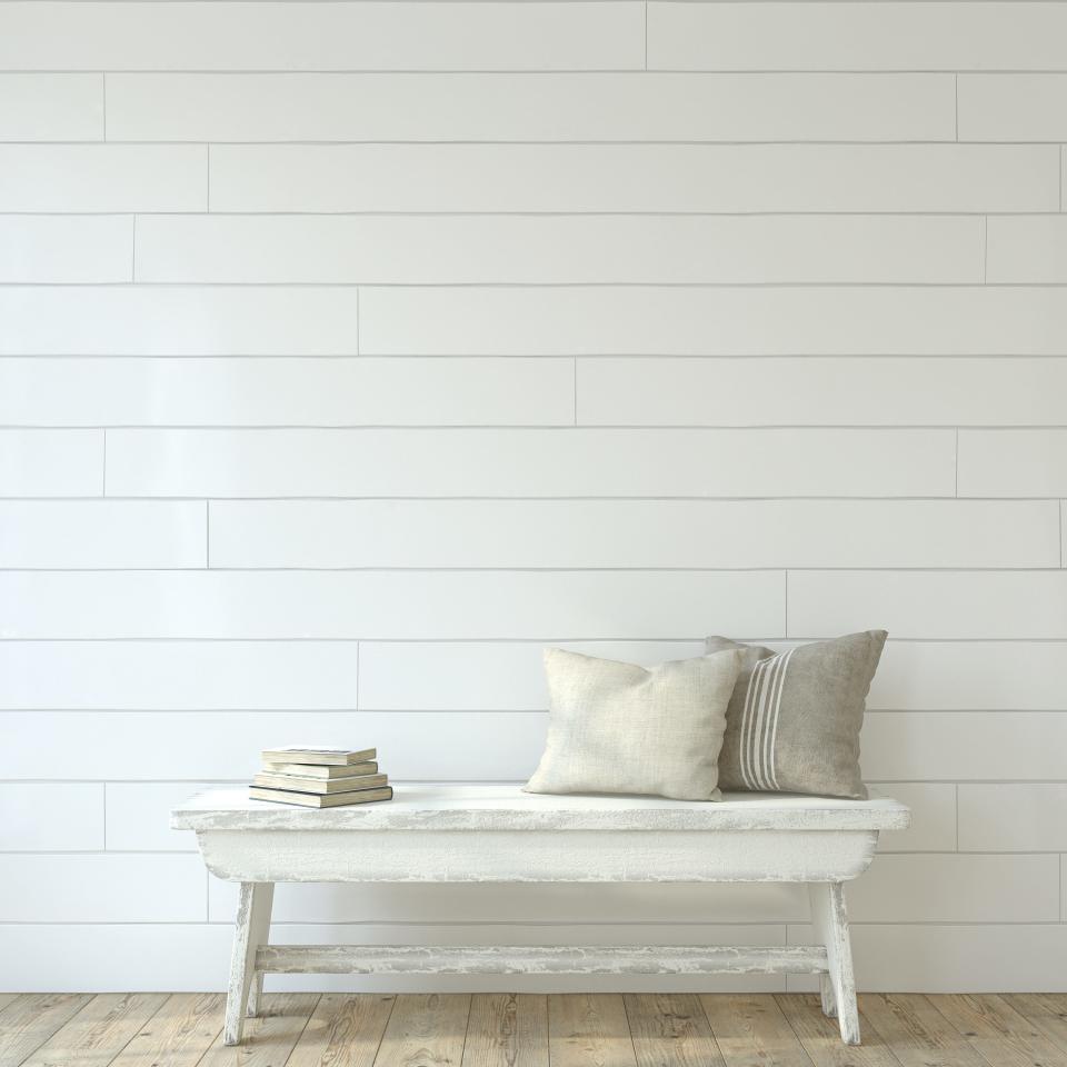 White shiplap wall with worn white bench with books with pages facing out and two white and gray pillows on bench