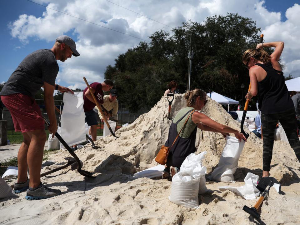 people with shovels fill white bags from a pile of sand