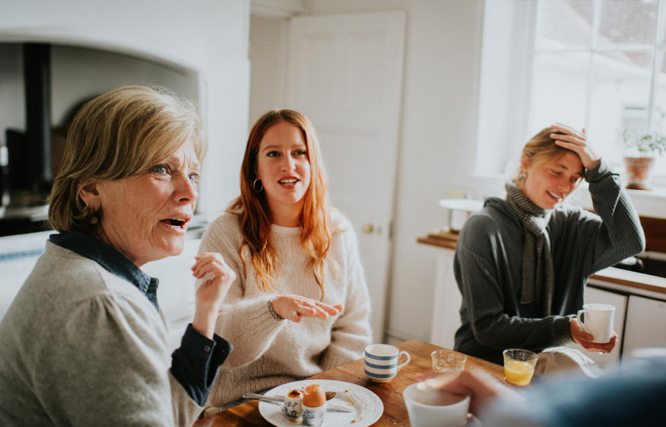 Three women in a cozy kitchen share a casual conversation over drinks and snacks