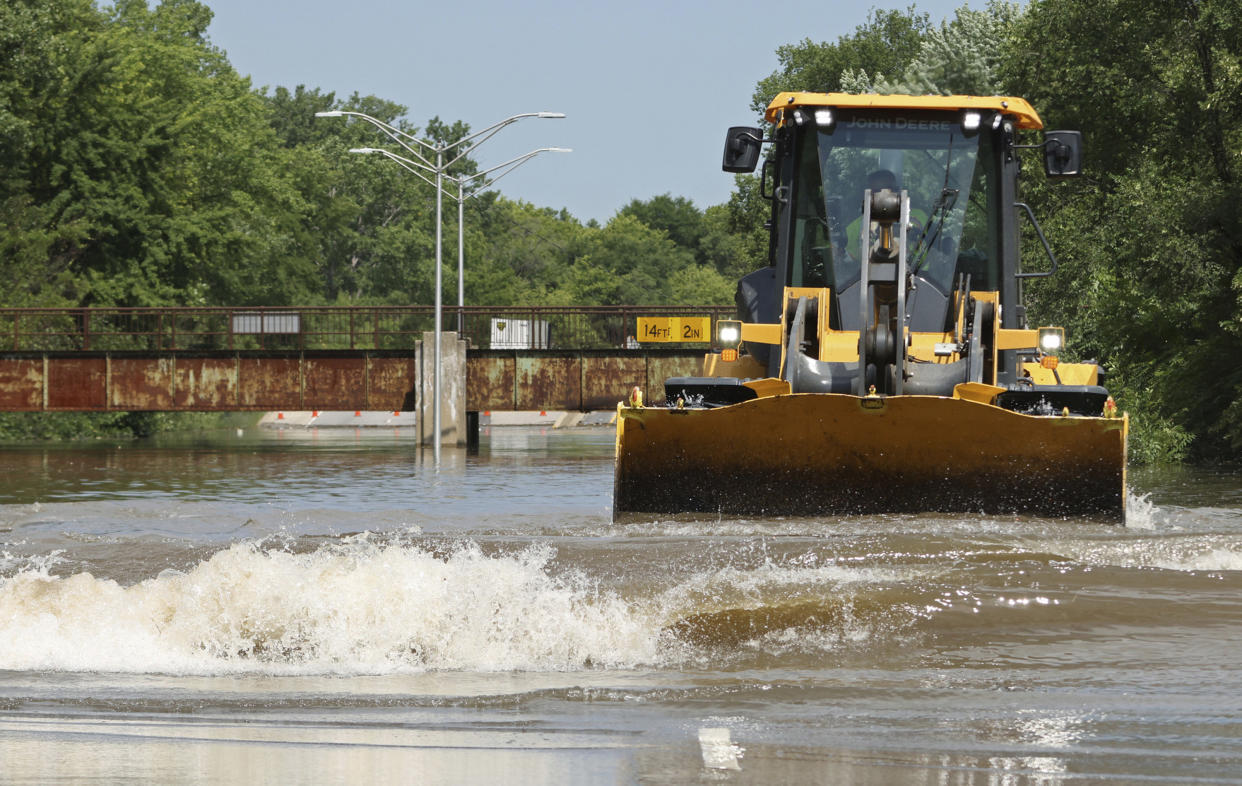 A worker driving a tractor moves water toward a storm drain after heavy rain.
