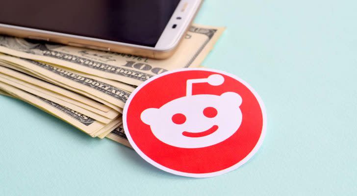 A Reddit sticker rests next to an iPhone and a pile of cash.