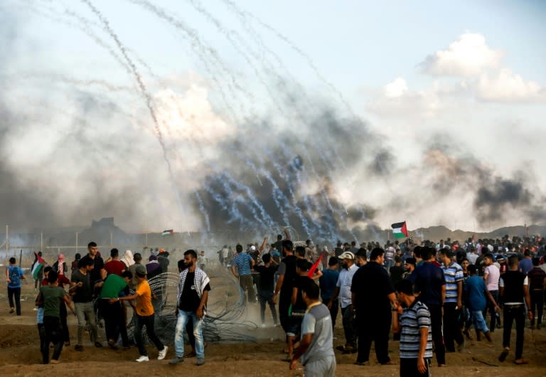 Palestinian protesters watch as tear gas grenades fired by Israeli forces fall during clashes following a demonstration along the Israel-Gaza border