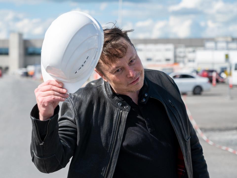 Elon Mush holds a Tesla-branded hard hat.