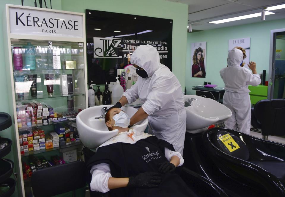 In this June 8, 2020 photo, a stylist, dressed in protective gear as a measure to curb the spread of the new coronavirus, washes a client's hair, in Medellin, Colombia. As COVID-19 cases surge in Latin America, the Colombian city of Medellin is defying expectations and managing to keep numbers remarkably low. (AP Photo/Luis Benavides)