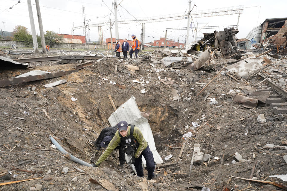 A Ukrainian policeman collects fragments in the crater to determine the type of ammunition after a Russian attack ruined a railway depot in Kharkiv, Ukraine, Wednesday, Sept. 28, 2022. (AP Photo/Andrii Marienko)