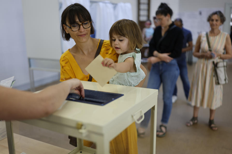 A girl casts the ballot for her mother at a voting station in Strasbourg, eastern France, Sunday June 12, 2022, Sunday, June 12, 2022. French voters are choosing lawmakers in a parliamentary election as President Emmanuel Macron seeks to secure his majority while under growing threat from a leftist coalition. (AP Photo/Jean-Francois Badias)