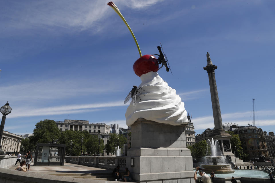 A woman take a photo on her smart phone of the new work of art entitled 'The End' by artist Heather Phillipson which was unveiled on the fourth plinth in Trafalgar Square in London, Thursday, July 30, 2020. Described as representing "exuberance and unease" and a "monument to hubris and impending collapse", The End, by British artist Heather Phillipson, will stay in place until spring 2022. (AP Photo/Alastair Grant)