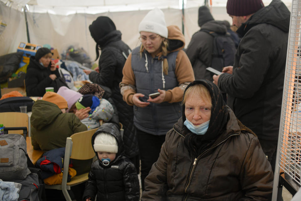 Refugees fleeing the conflict from neighbouring Ukraine warm up inside a tent at the Romanian-Ukrainian border, in Siret, Romania, Saturday, March 5, 2022. (AP Photo/Andreea Alexandru)