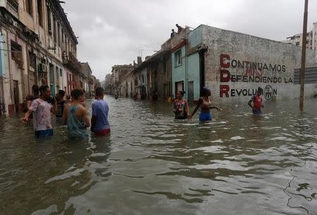 People wade through a flooded street, after the passing of Hurricane Irma, in Havana, Cuba September 10, 2017. The sign on the wall reads "We will continue to defend the revolution." REUTERS/Stringer