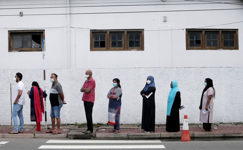 People wearing protective masks wait in a line outside a polling station as they prepare to cast their vote during the country's parliamentary election in Colombo