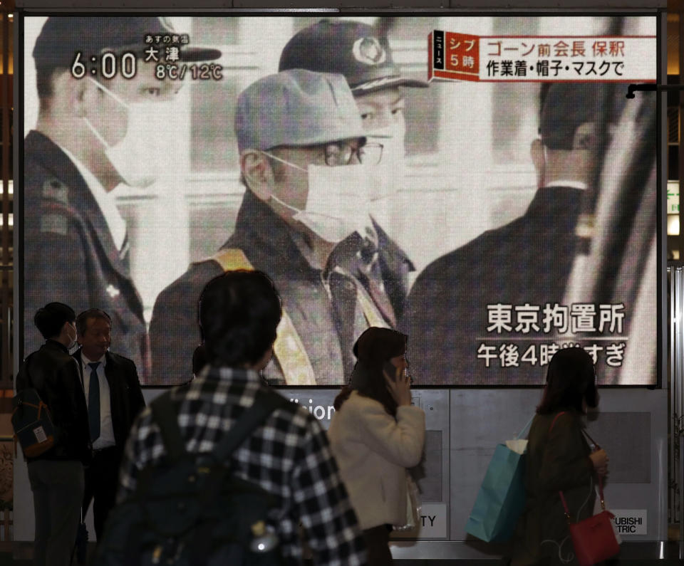 People walk by a monitor which reports on the bail of former chairman of Nissan Motor Co., Carlos Ghosn, in Osaka, western Japan Wednesday, March 6, 2019. Disguised as a construction worker, Ghosn left a Tokyo detention center Wednesday after posting 1 billion yen ($8.9 million) bail. The letters, top right, read " Ghosn released. Construction worker's outfit, hat and mask. " (Kyodo News via AP)