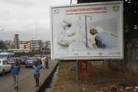 People walk past a billboard displaying a government message about Ebola, which reads: "The risk of Ebola is still there. Let us apply the protective measures together", on a street in the capital Abidjan September 10, 2014. REUTERS/Luc Gnago