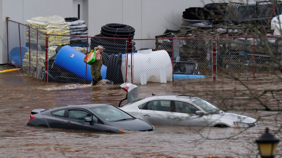 A man wearing chest waders walks past cars abandoned in floodwaters in a mall parking lot in Halifax, Nova Scotia, on Saturday. - Darren Calabrese/The Canadian Press/AP