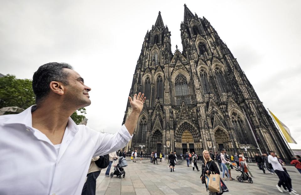 Fadel Alkhudr from Syria poses near the word heritage Cologne Cathedral in Cologne, Germany, Monday, June 20, 2022. Fadel Alkhudr, 42, a woodcarver and artist orginally from Aleppo, Syria, fled the war in his home country and arrived in the western german city of Cologne in 2015. In 2019 he started to carve the local Cologne Cathedral in his small basement - without any plans or drawings, using only cell phone photos of the cathedral as a template. (AP Photo/Martin Meissner)