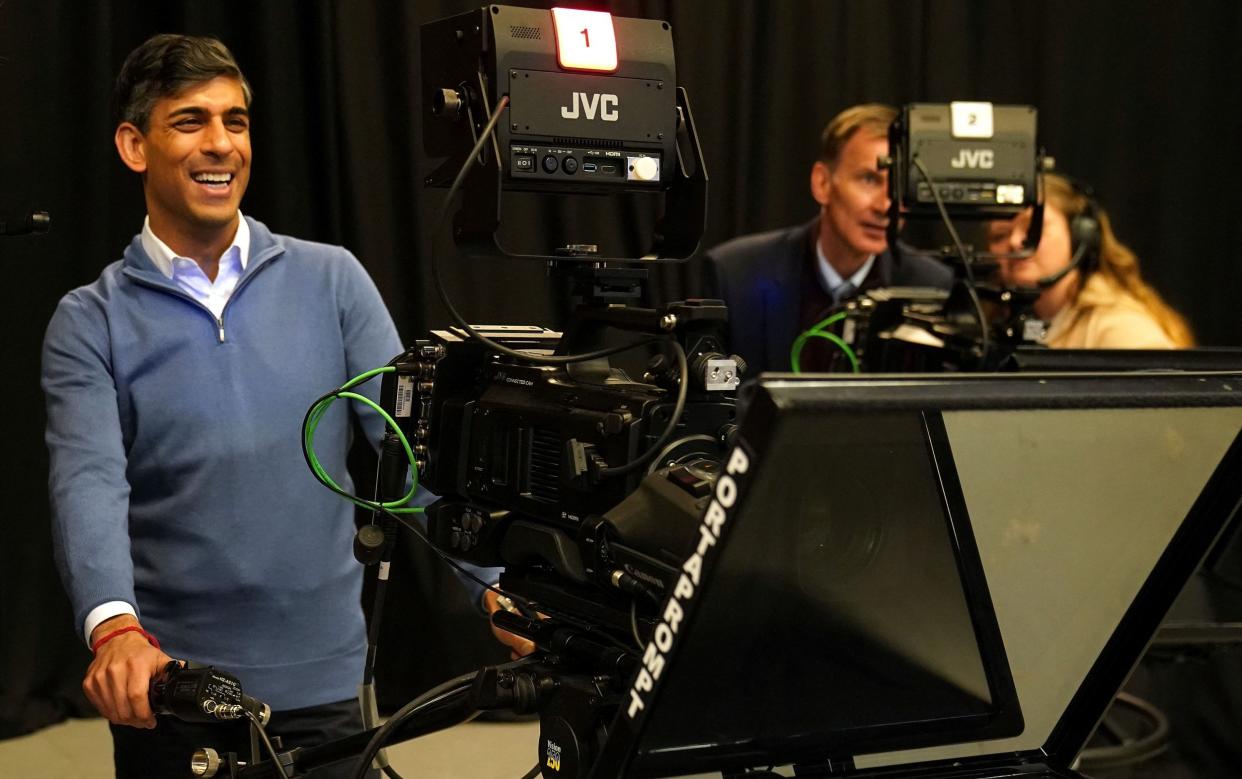 Rishi Sunak in casual clothes using a large camera, while Jeremy Hunt speaks to a camera operator behind him