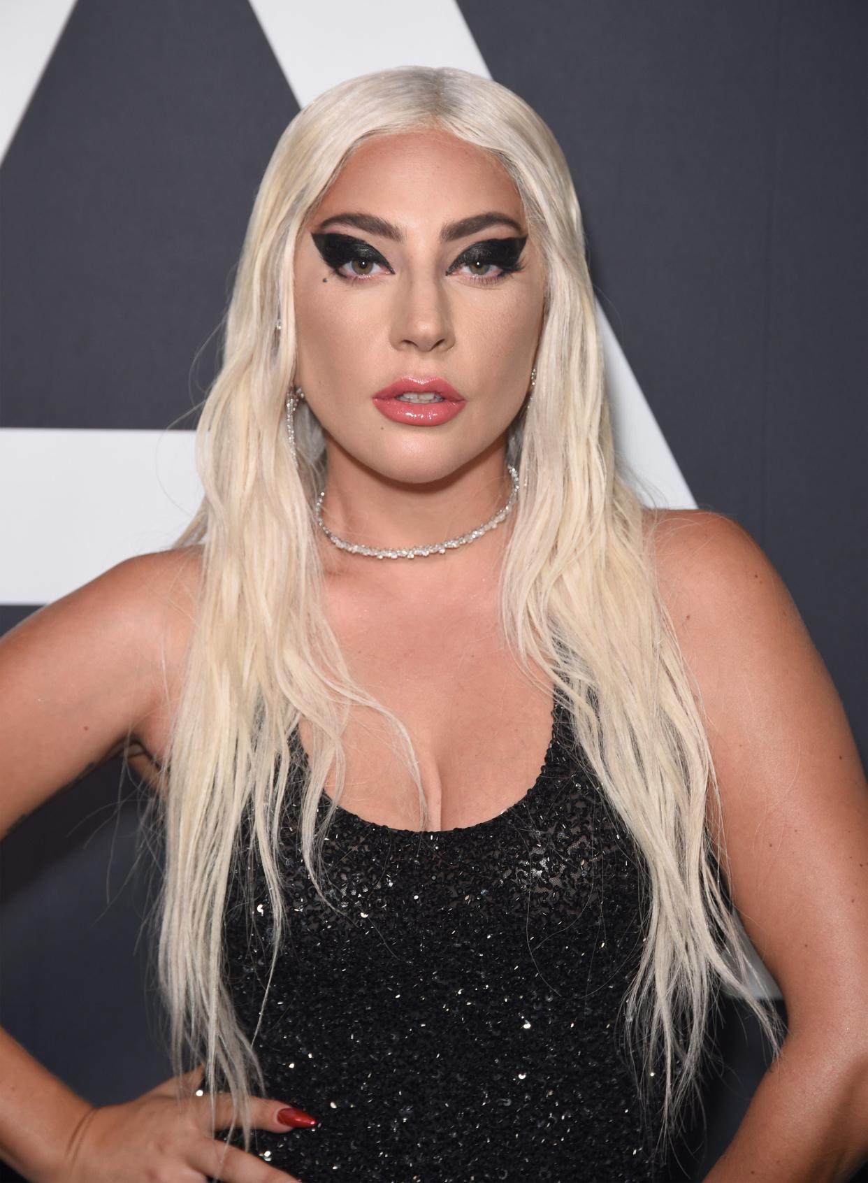 Lady Gaga poses wearing dark winged eye makeup and a sparkly black tank top