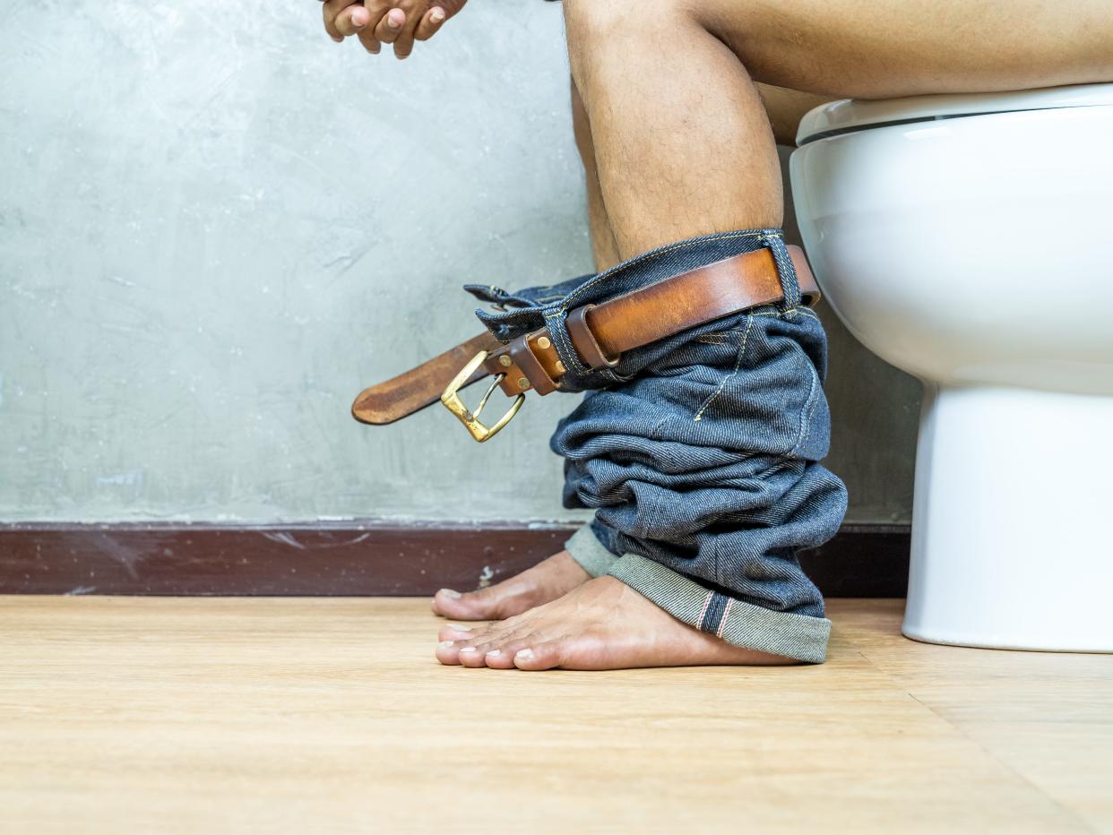 Man sitting on toilet with pants around his ankles