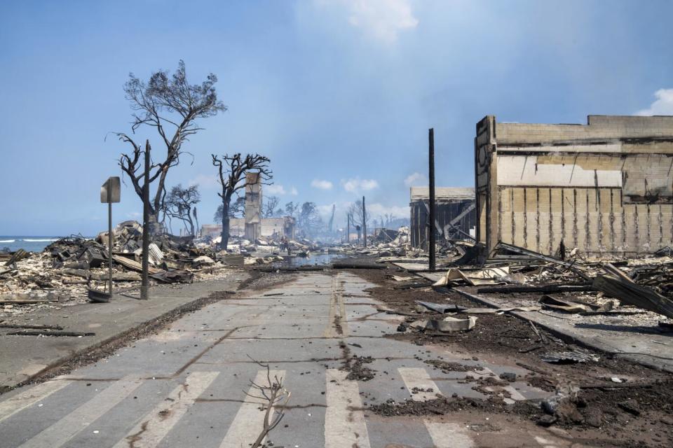 Rubble and portions of burned-out buildings border a roadway.