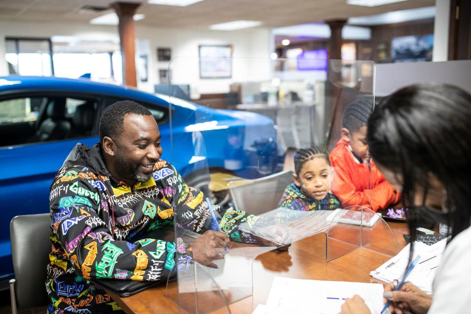 Jay Adams Chesterton, Ind., next to his sons Sebastian, 7, and Trey, 8, signs a leasing agreement with new car sales specialist Sherry Porter at the Village Ford in Dearborn on Feb. 2, 2022.