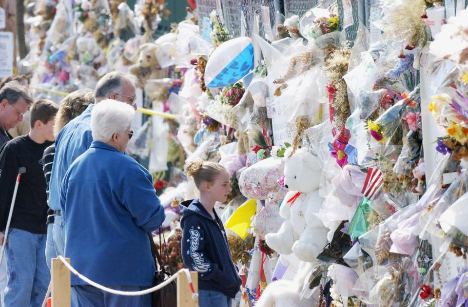 People look over the thousands of mementos that were left on the fence surrounding the remains of The Station nightclub.
