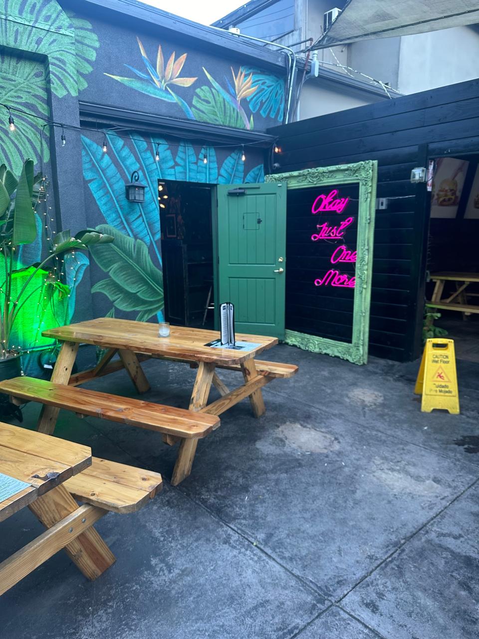 Outdoor seating area with wooden benches and a neon sign on a door