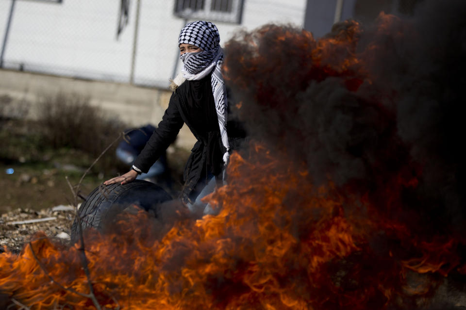 A masked Palestinian protester sets tires on fire during clashes with Israel forces as they protest Middle East peace plan announced Tuesday by US President Donald Trump, which strongly favors Israel, at Beit El checkpoint, near the West Bank city of Ramallah, Wednesday, Jan 29, 2020 (AP Photo/Majdi Mohammed)