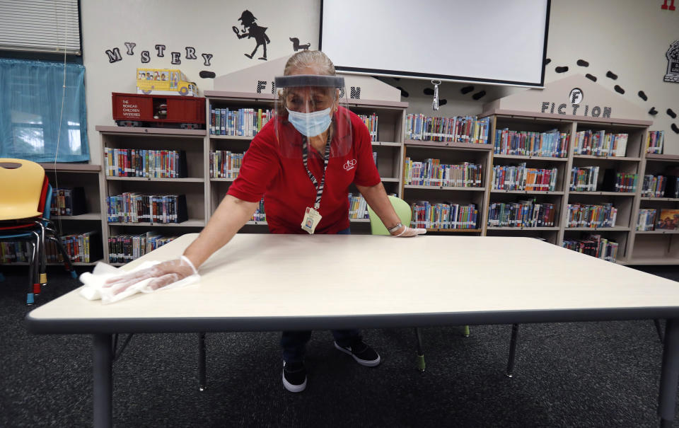 Wearing a mask and face guard as protection against the spread of COVID-19, Garland Independent School District custodian Camelia Tobon wipes down a table in the library at Stephens Elementary School in Rowlett, Texas, Wednesday, July 22, 2020. (LM Otero/AP)