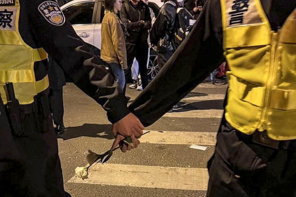 2022年11月27日凌晨，警察圍堵上海烏魯木齊中路聚集的大量市民，其中兩名警察共同手執一支白花。