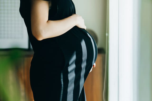 <p>Getty Images</p> Pregnant woman standing by a window