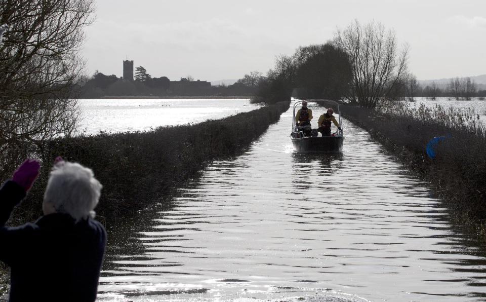 In this photo taken Sunday Feb. 2, 2014, an emergency services boat comes along one of the flooded roads from Muchelney in Somerset, England, to pick up a resident and take them to the village, which has been cut off by road since Jan. 1 this year. Here on the Somerset Levels _ a flat, marshy region of farmland dotted with villages and scored by rivers and ditches _ it's often wet. But not this wet. Thousands of acres of this corner of southwest England have been under water for weeks, some villages have been cut off for more than a month, and local people forced to take boats to get to school, work and shops are frustrated and angry. Some blame government budget cuts and environmental bureaucracy. Others point to climate change. Even plump, endangered water voles are the target of ire. (AP Photo/Alastair Grant)