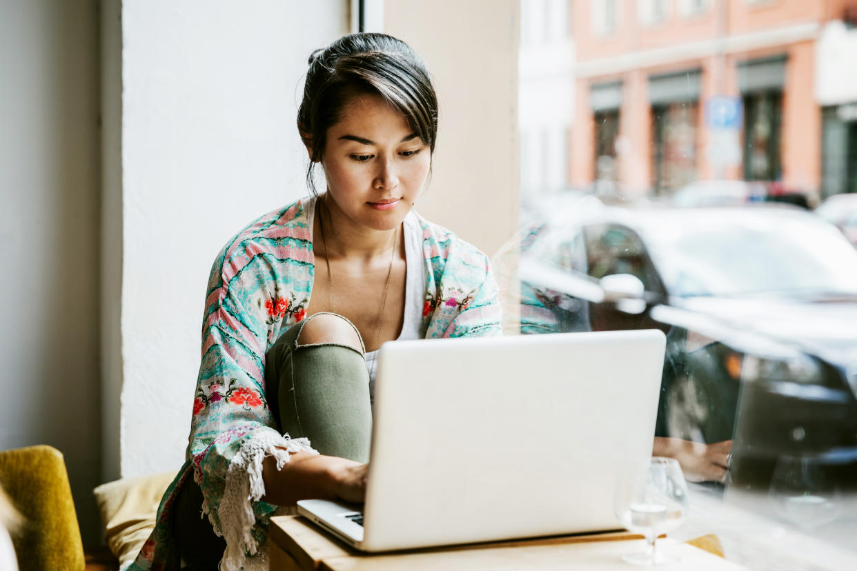 A young woman sitting at the window in a cafe and working from her laptop.