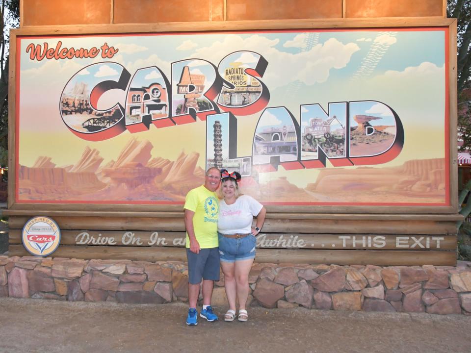 dana and a friend posing in front of the cars land sign at disneyland