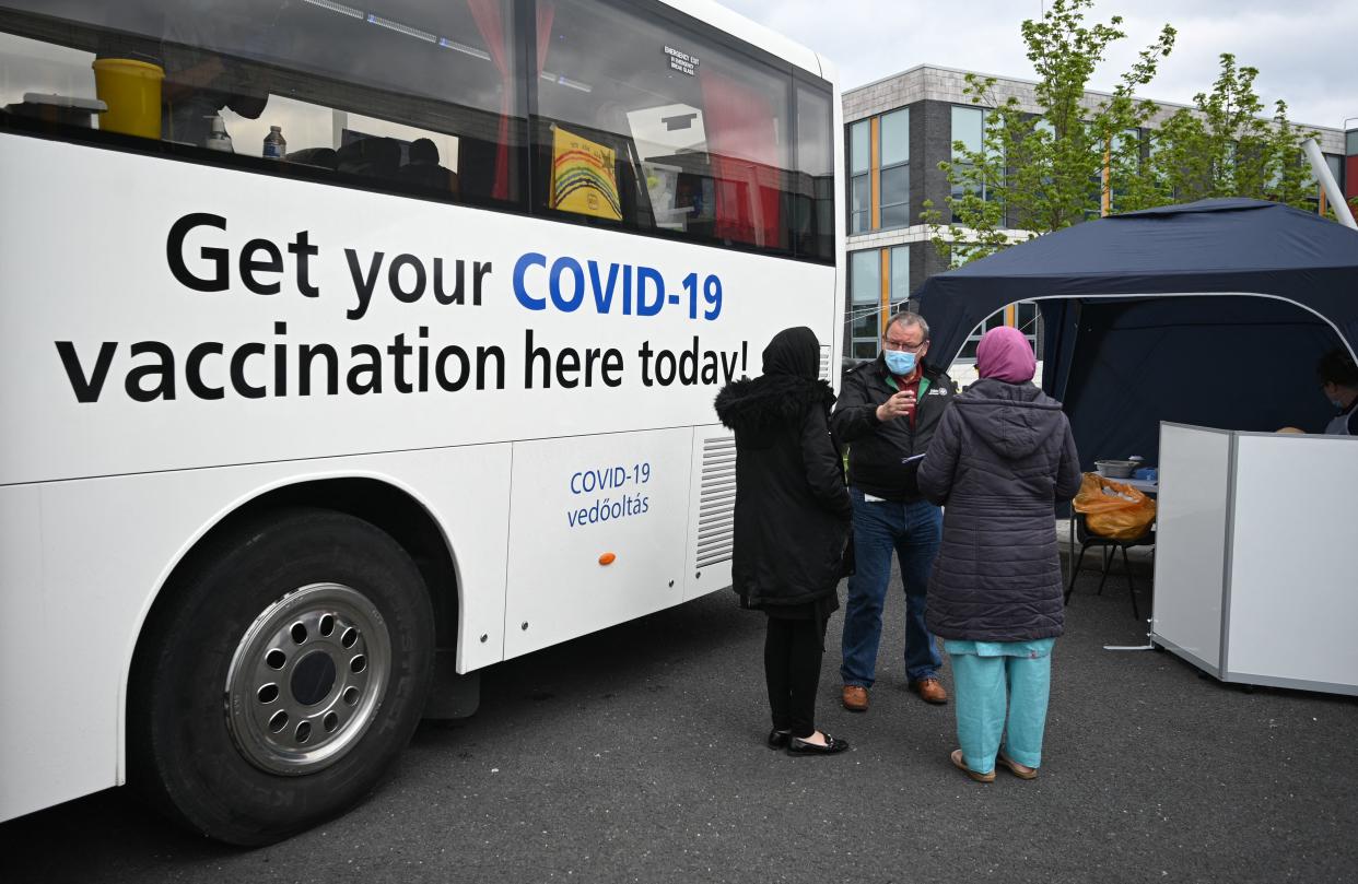 People stand by Covid-19 vaccination-branded coach parked at a temporary vaccination centre at the Essa academy in Bolton, northwest England on May 14, 2021. - England remains on track for the latest easing of its coronavirus lockdown next week but is taking no chances after a doubling of cases of an Indian variant, the government said today. (Photo by Oli SCARFF / AFP) (Photo by OLI SCARFF/AFP via Getty Images)