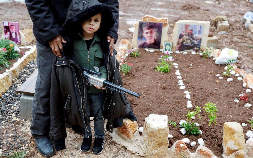 A young boy holds a toy gun at a family-member's grave