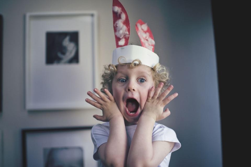 small curly headed child wearing homemade bunny ears who might be acting out a charades prompt after an easter egg hunt